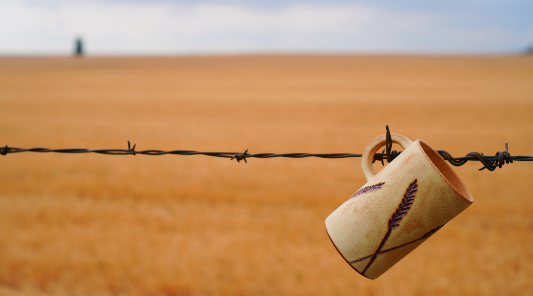 Handmade Stoneware Ceramic Mug, with carved sgraffito Wheat design & Jug Handle, hanging from barbed wire in wheat field